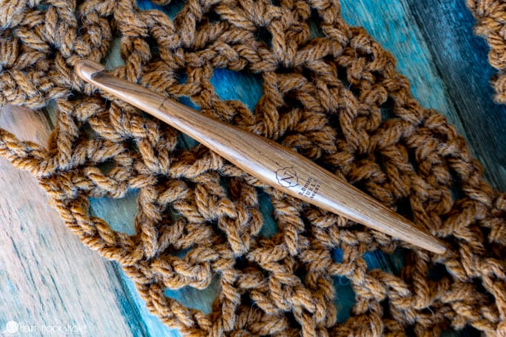 Wood crochet hook laying on a sample of the Afternoon Scarf crochet pattern in Hue + Me yarn from Lion Brand in the “Arrowwood” colorway.