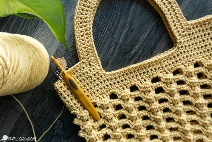 Gold colorway of a sample of the Bobbles for Baubles Bag crochet pattern with a crochet hook laying on top.