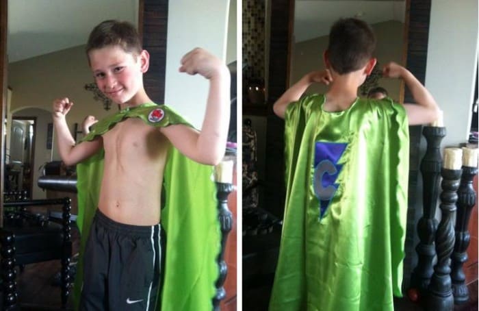 Smiling male child wearing a green superhero cape.