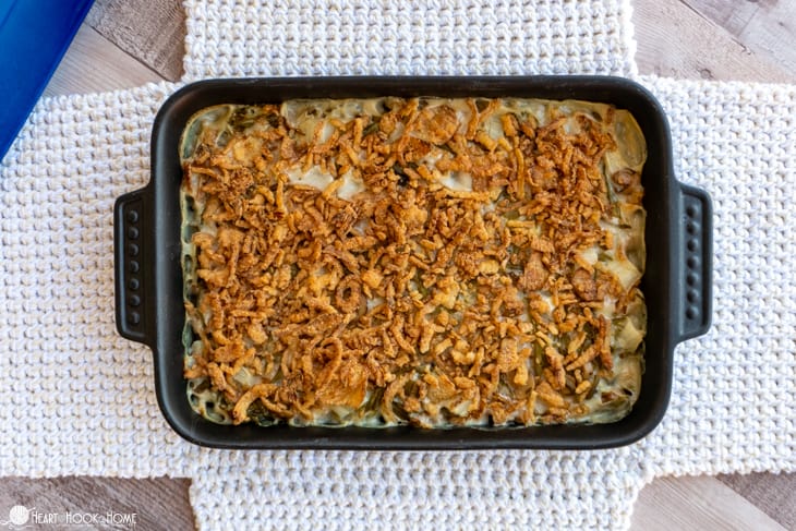 Green Bean Casserole in a black pan laying on an example of a white Casserole Carrier crochet pattern.