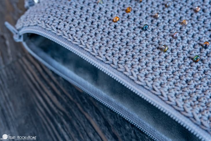 Gray sample of the Cross-Body Bead Bag crochet pattern with natural colored beads laying on its side with the zipper and lining showing.