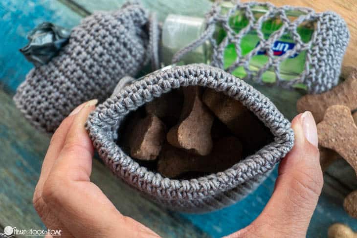 Gray colorway of an example of the Dog Treat Bag crochet pattern with dog treats peaking out and being held open by a hand.