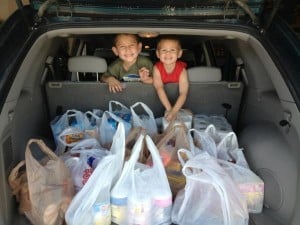 Two smiling boys leaning on a backseat with the cargo area full of bags of donation items.