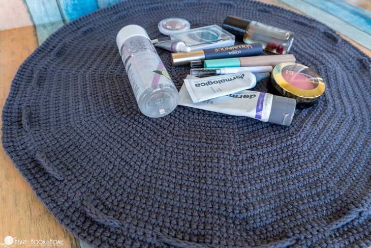 Example of a gray Drawstring Cosmetics Bag crochet pattern laid flat with various cosmetics in the middle.