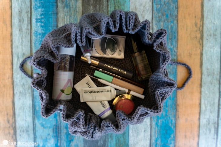 Example of a partially open, gray Drawstring Cosmetics Bag crochet pattern with various make up containers inside.