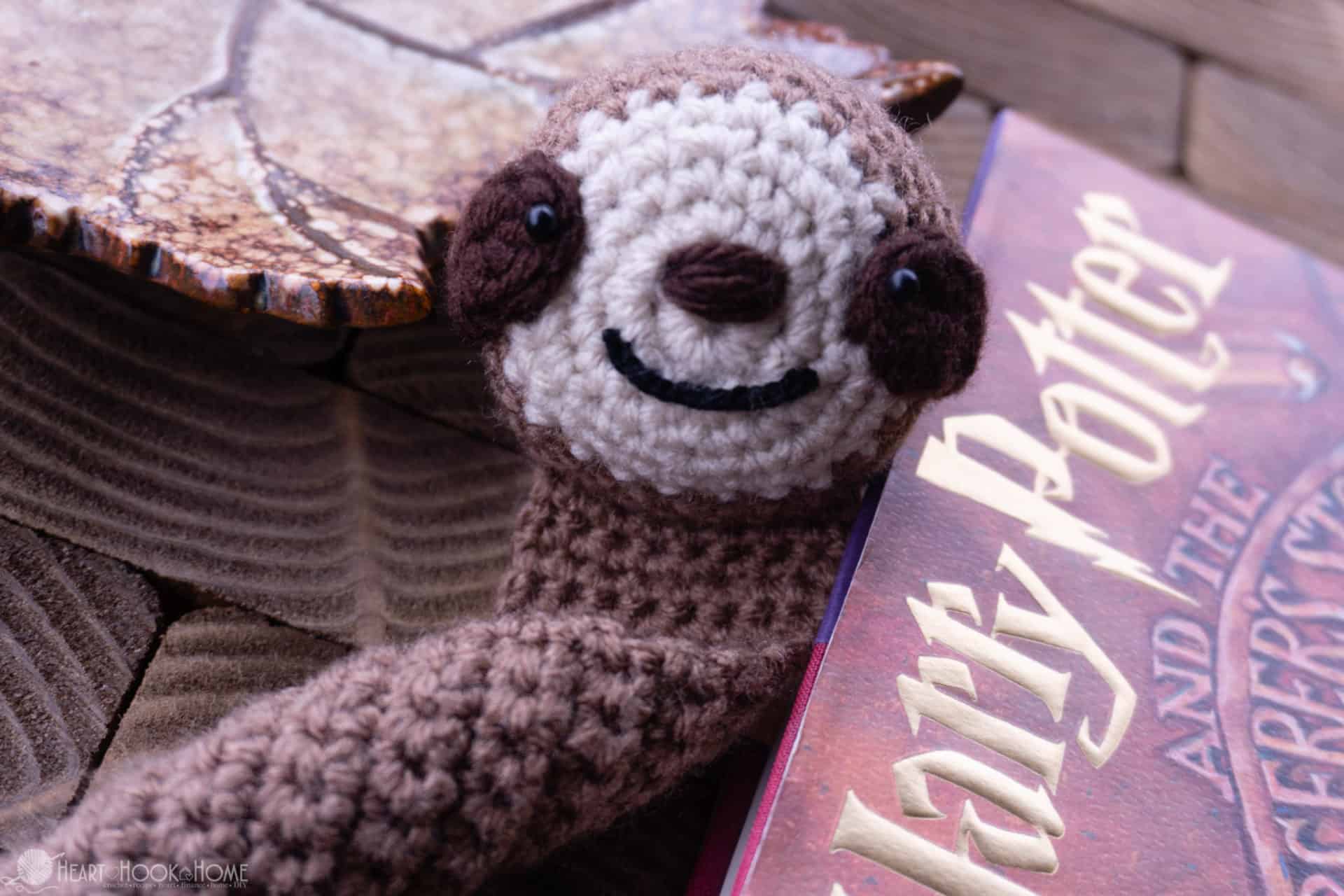 Brown and tan example of the Samson the Sloth Bookmark crochet pattern next to a Harry Potter book.