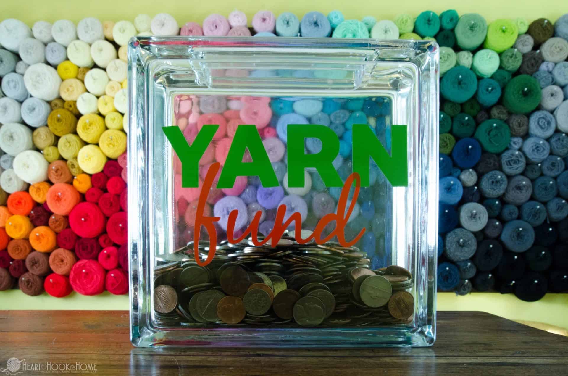 Partially full of money example of the Yarn Fund DIY Piggybank with a colorful yarn wall in the background. 