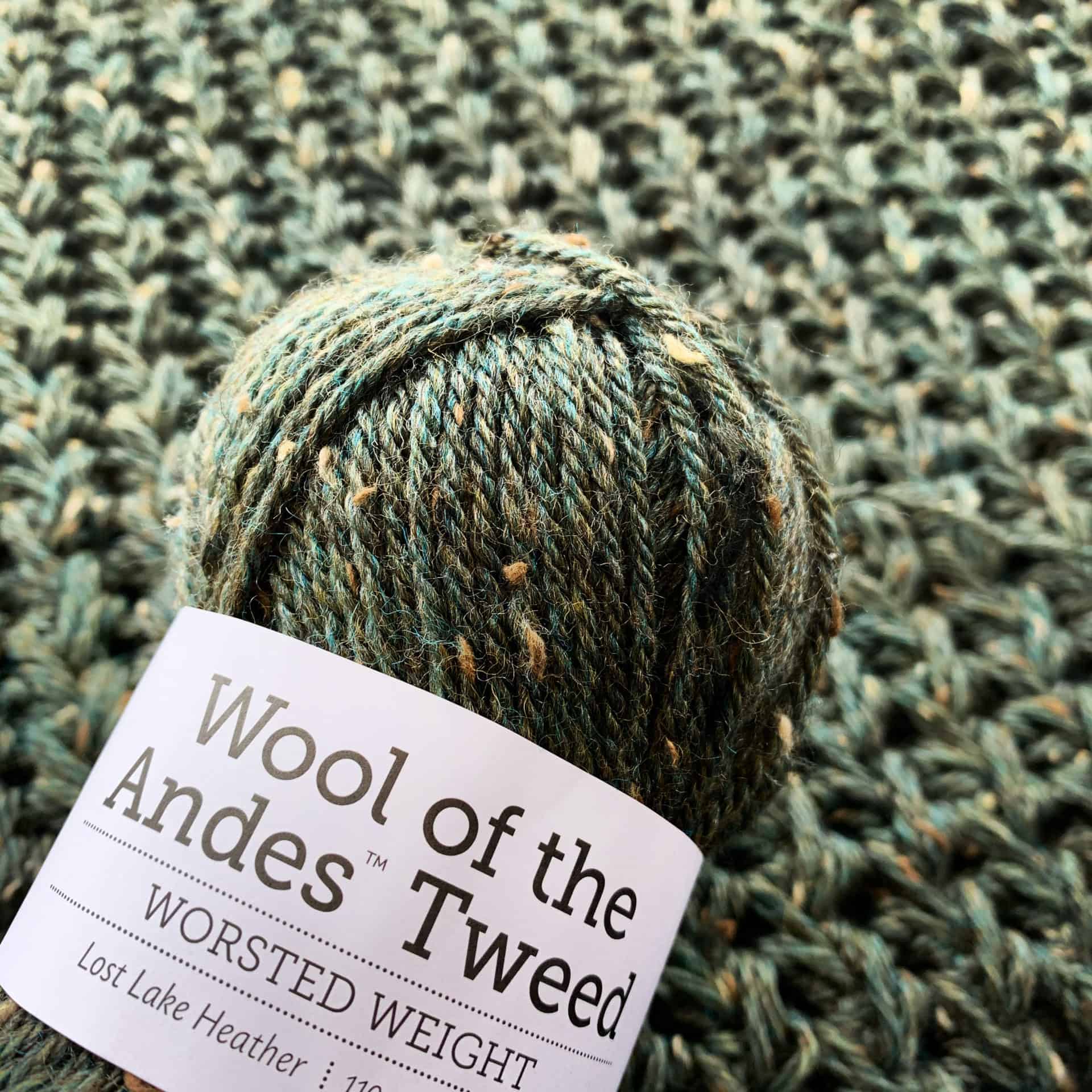 Skein of Knit Picks Wool of the Andes Tweed (worsted weight yarn) in Lost Lake Heather colorway on a sample of the Cordillera Cape crochet pattern.