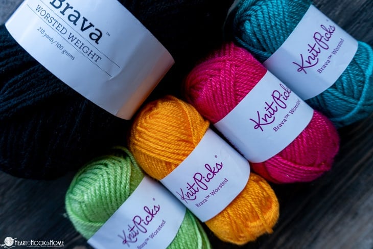 Brava Mini skeins of yarn in green, orange, pink, and blue next to a black Brava worsted weight skein of yarn.