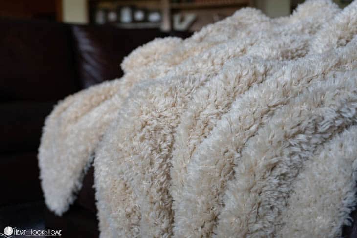 White example of the Faux Fur Throw crochet pattern draped over a leather couch.