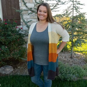 Example of a white, yellow, orange, and blue colorway of the Grid Cardi  on a smiling female model standing in a front yard setting.