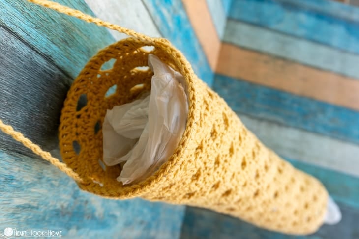 Top of an example of a gold colorway of the Plastic Bag  Holder and Dispenser crochet pattern showing a plastic sack stuffed inside.