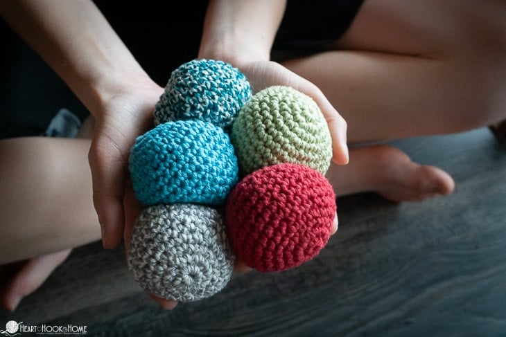 Multiple examples of various colors of the Hacky Sack crochet pattern being held in hands.