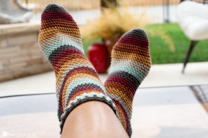 Modeled on a pair of crossed feet is an example of the Herringbone Socks crochet pattern in striped fall colors.