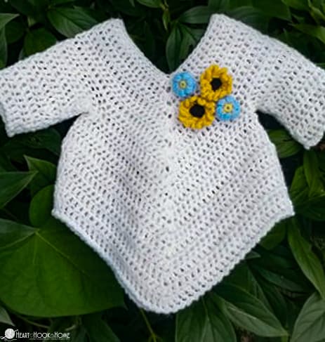 White example of the 9/12 month size of the On Point Poncho crochet pattern with small crocheted flowers on the front.