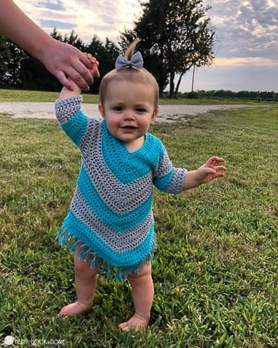 Gray and blue example of the 12/18 month size of the On Point Poncho crochet pattern on a small child in a park setting.