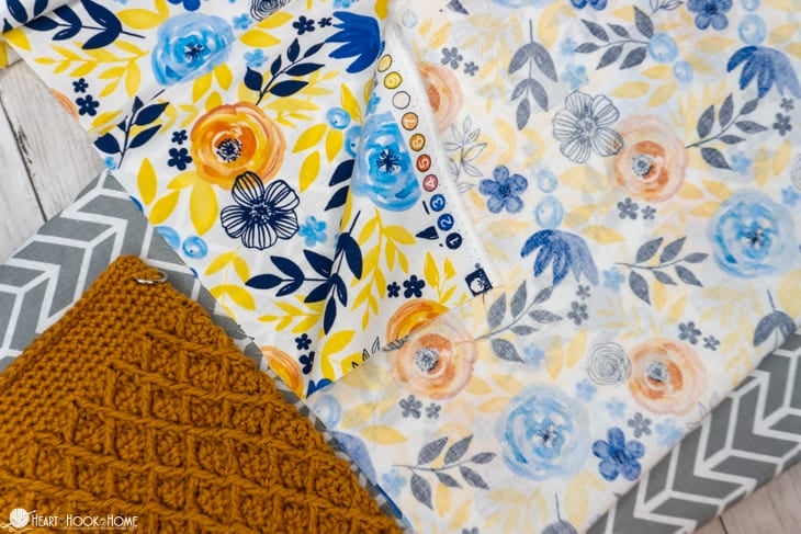 Flowery fat quarter lining laid on top of a gold colorway example of the Girl\'s Best Friend Crossbody Purse crochet pattern.