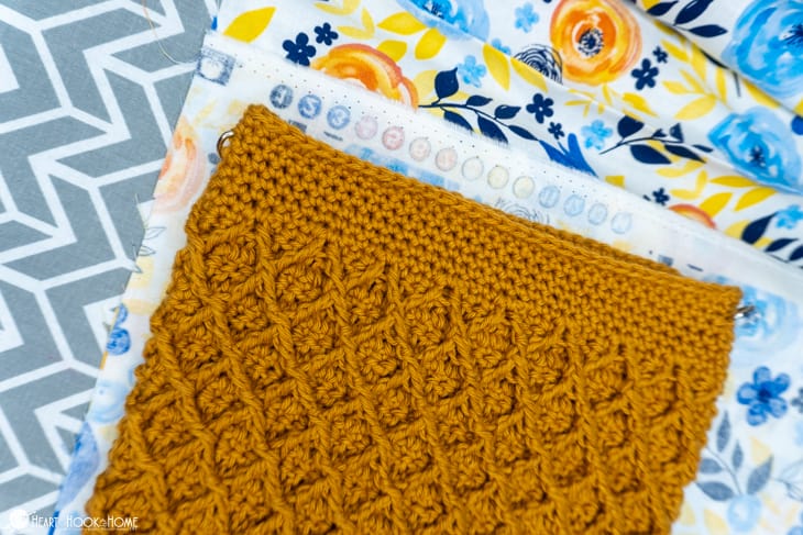 Gold colorway example of the Girl\'s Best Friend Crossbody Purse crochet pattern laid on top of a flowery fat quarter lining.
