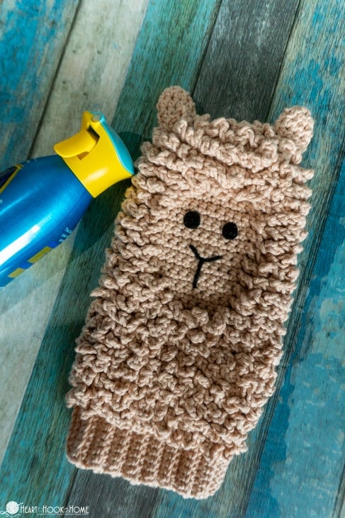 Tan colorway example of the Llama Dusting Mitt crochet pattern next to a bottle of dusting spray.