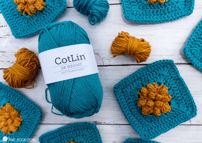 Examples of the Marigold Sky Granny Square crochet pattern in a Mustard Seed and Surf colorway of Cotlin Yarn next to a skein of Cotlin Yarn in Surf colorway.