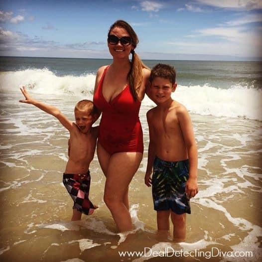 Female model with her arms around her young sons while standing in the ocean with waves in the background.