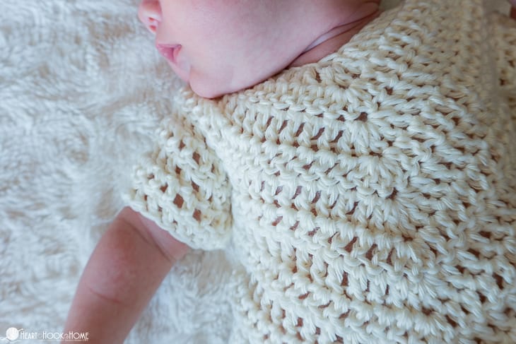 Ivory example of the newborn size of the On Point Poncho crochet pattern on a baby laying on a blanket.
