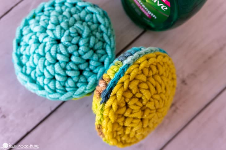 Examples of the Pot Scrubber crochet pattern in a teal and yellow colorway next to a bottle of dish soap.