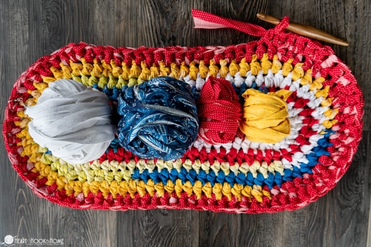 Red, white, blue, and yellow colorway example of the Rag Rug crochet pattern with rolls of strips of fabric laying on top.