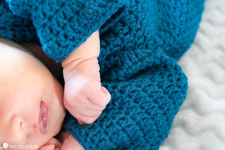 Infant wearing a blue example of the Simple Newborn Sleeper Crochet Pattern