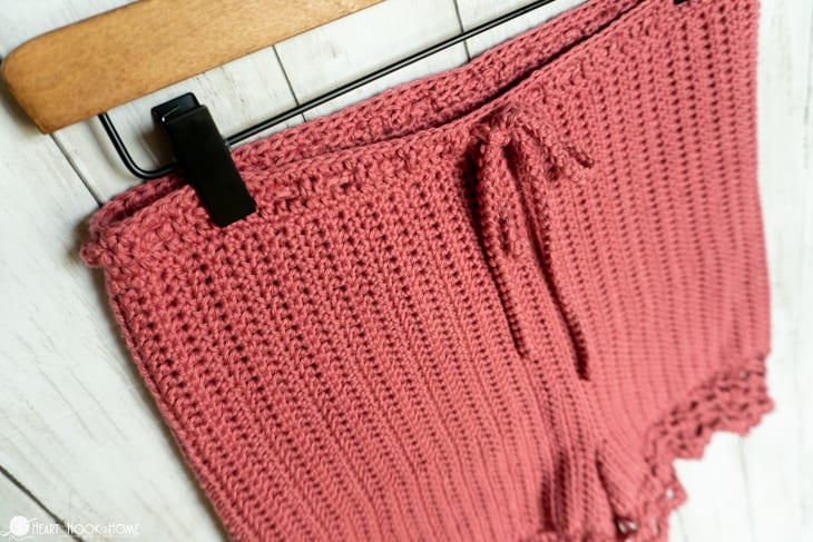 Up close of the drawstring on a peony colorway of the Staycation Shorts crochet pattern on a wooden hanger.