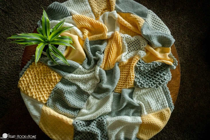 Silver, white, and gold example of the Crochet Stitch Sampler Afghan Pattern next to a green plant.