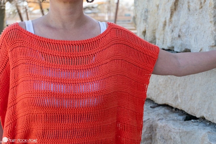 Example of the Track Stitch Tunic crochet pattern made with Shine Sport Yarn in the Grapefruit colorway on a female model standing in front of a stone wall.