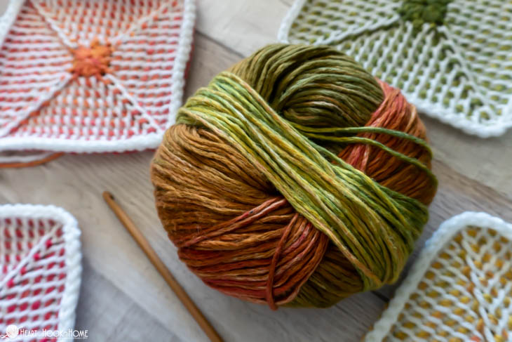 Multiple colored examples of the Tunisian Crochet Granny Square pattern, a multi colored ball of yarn, and a wood crochet hook.