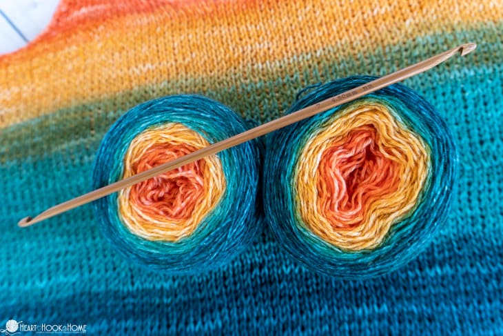 KnitPal Bamboo Double Ended Tunisian Crochet Hook laying across 2 skeins of Stroll Gradient yarn in the “Camper Van” colorway with a sample of the Tunisian Sunrise Crochet Tank Top in the background.