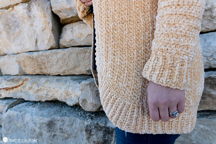 Soft Sunshine colorway example of the Velvet Cardi Crochet Pattern on a female model standing in front of a brick wall.