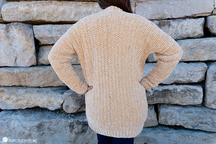 Soft Sunshine colorway example of the Velvet Cardi Crochet Pattern on a female model standing in front of a brick wall.