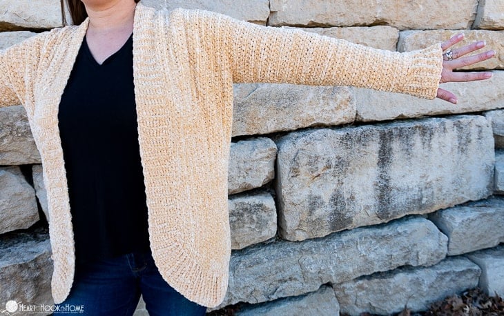 Soft Sunshine colorway example of the Velvet Cardi Crochet Pattern on a female model standing in front of a brick wall.