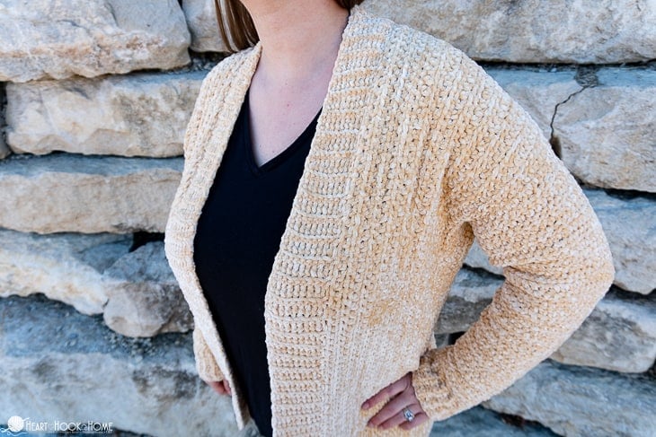 Soft Sunshine colorway example of the Velvet Cardi Crochet Pattern on a female model standing in front of a brick wall.
