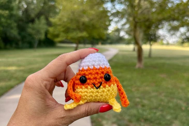 Example of Carl the Candy Corn crochet pattern being held by a hand in a park setting.