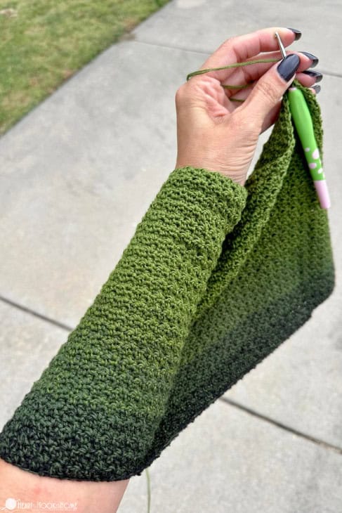 Green colorway of a crochet sample draped over an arm holding a crochet hook.