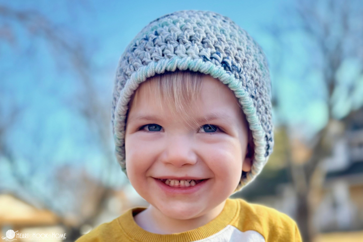 Blue variegated example of the Child Size Easy 30-Minute Beanie crochet pattern on a smiling male child. 