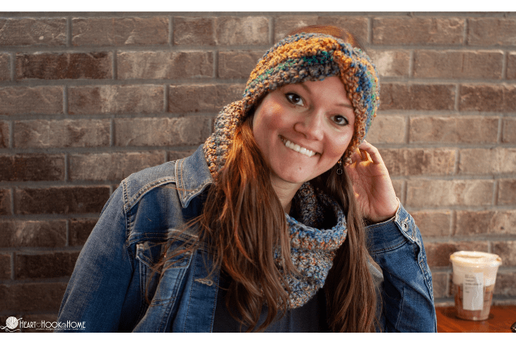Multicolored example of the Easiest Crochet Cowl pattern on a smiling model wearing a jean jacket in front of a brick wall.  