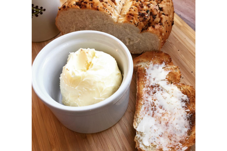 Homemade butter in a ramekin with crusty bread nearby with a smear of butter on it.  