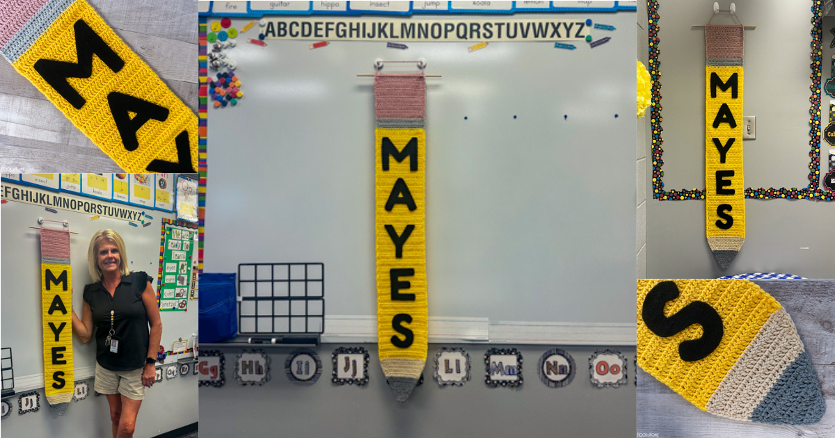 Pink, gray, yellow, and brown example of the Pencil crochet pattern hanging from a dry erase board in a classroom setting with the name Mayes on it in black.